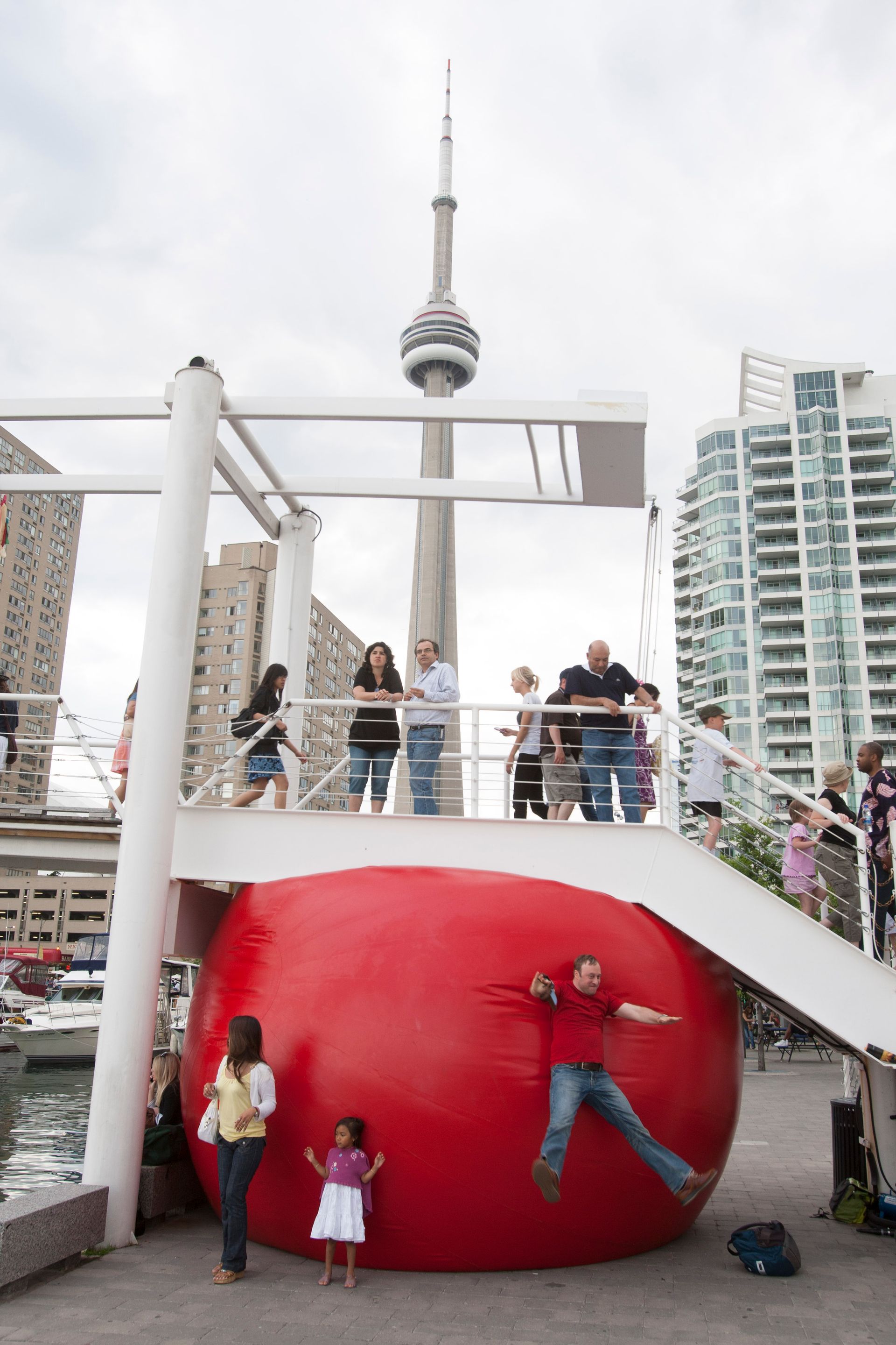 People interacting with a large red inflatable ball; CN Tower in background.