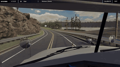 Driver’s view of a winding mountain road beside water under cloudy skies