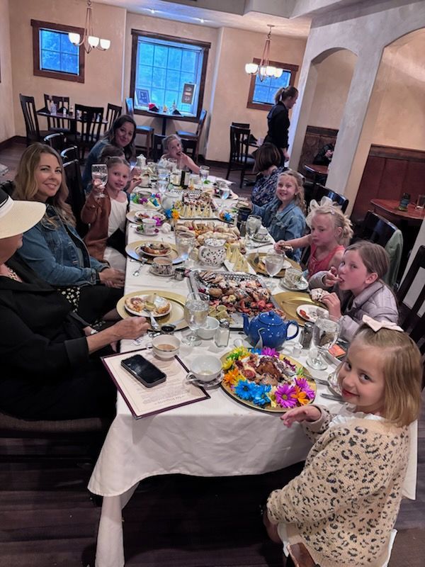 Group of people, mostly girls, at a long table set for a party in a restaurant. Smiles, food, drinks.