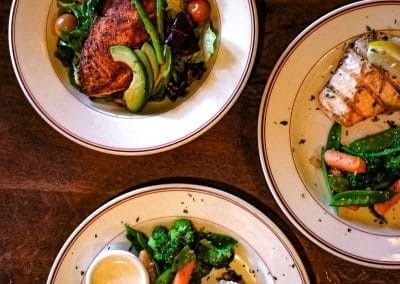 Three plates of food are sitting on a wooden table.