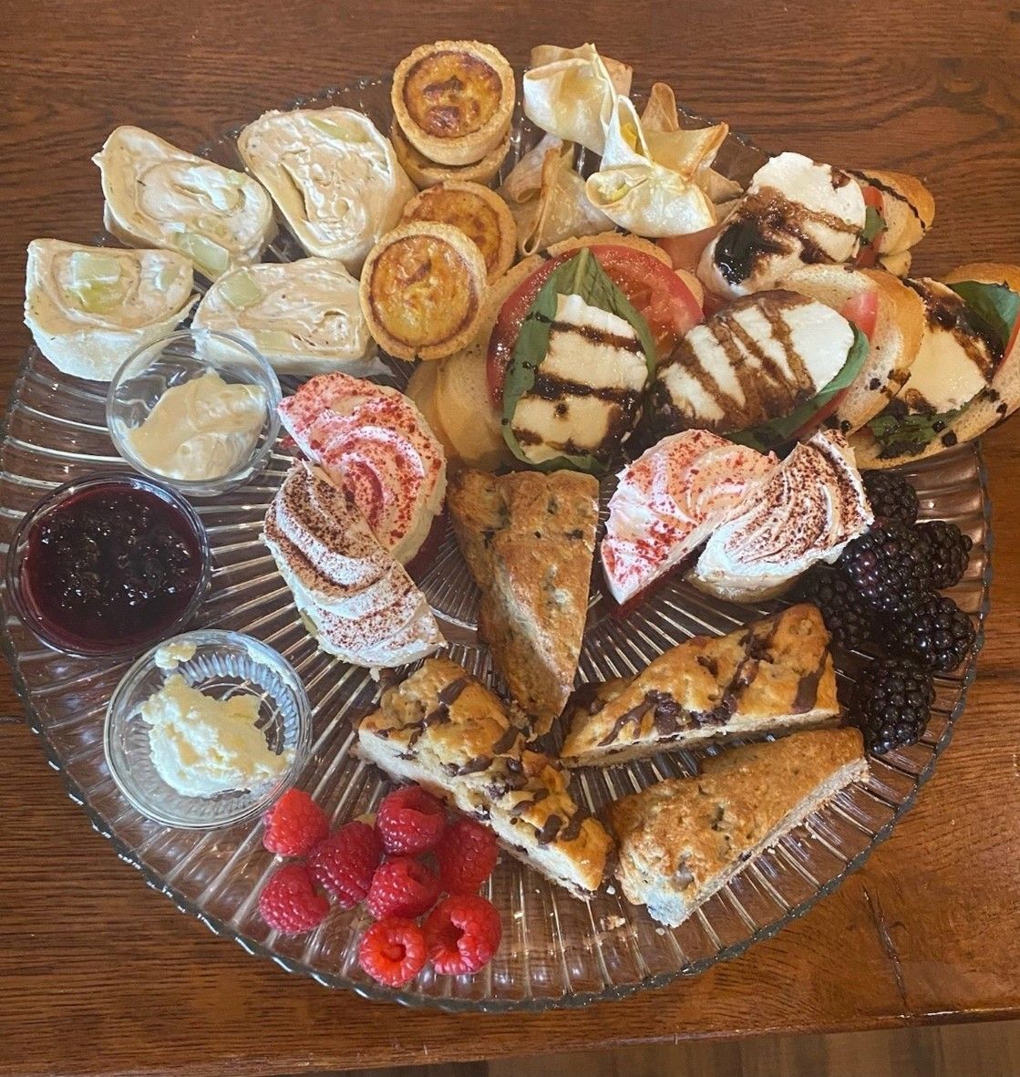 Assorted pastries, cookies, and fruit arranged on a glass platter on a wooden table