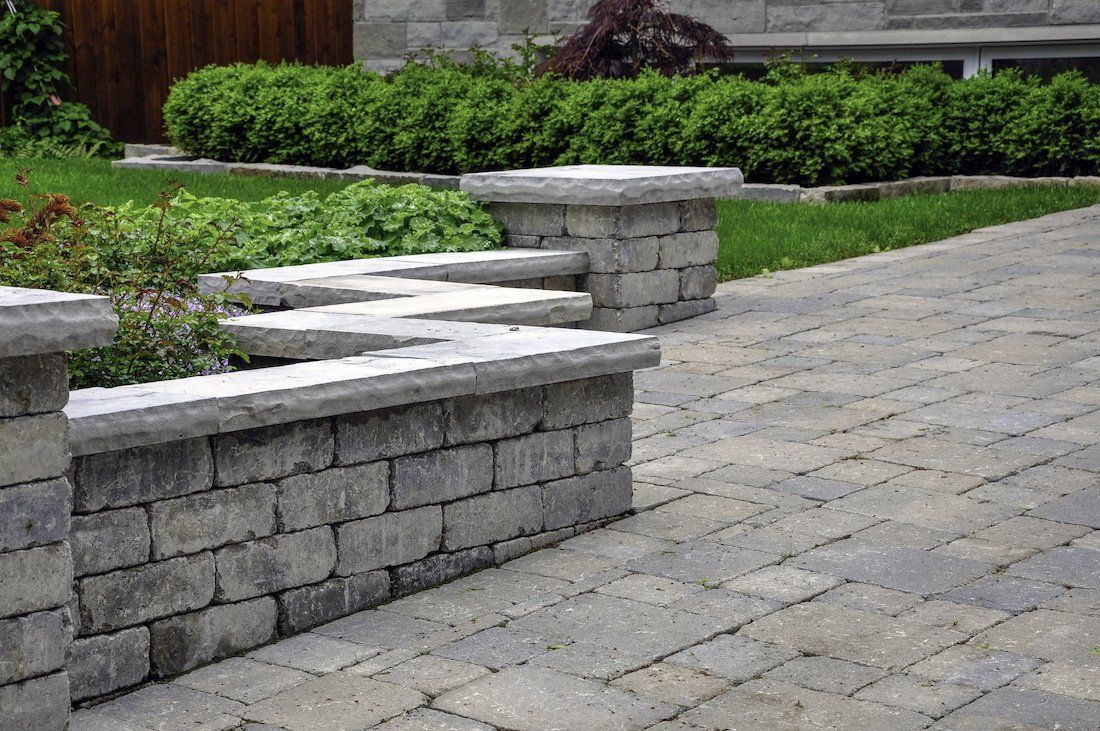 Stone retaining wall and paved walkway in a landscaped garden with trimmed hedges.