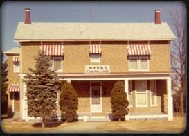 Front view of a beige two-story storefront with striped awnings and a Myers sign.