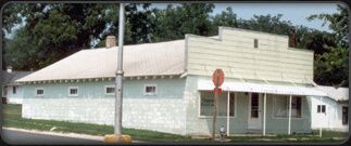 Small white building with a metal roof, front porch, and stop sign at the corner by trees