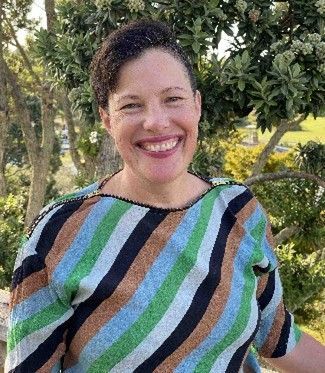 A woman in a striped shirt is smiling in front of a tree. Anna Kingston