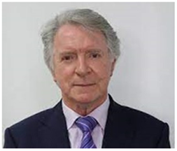 A man in a suit and tie is standing in front of a white wall. Bill Butler