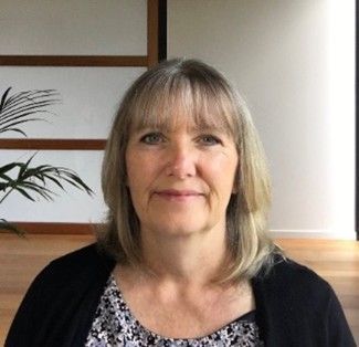 A woman is sitting in a room with a plant in the background and smiling at the camera. Jane Welch.