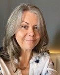 A woman with gray hair is smiling and wearing a white shirt. Lizzie Brandon