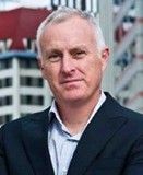 A man in a suit and white shirt is standing in front of a building. Professor Stephen Cummings
