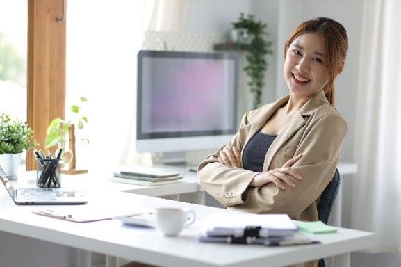 A woman is sitting at a desk with her arms crossed in front of a computer.
