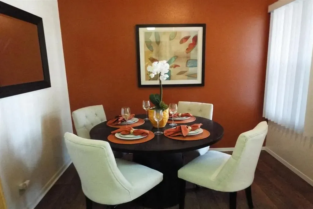 Dining area with a round table set for four, featuring white chairs and orange accents.