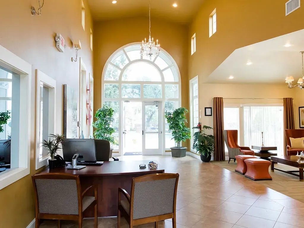 Reception desk and seating area in a high-ceilinged lobby with large arched windows and glass doors.