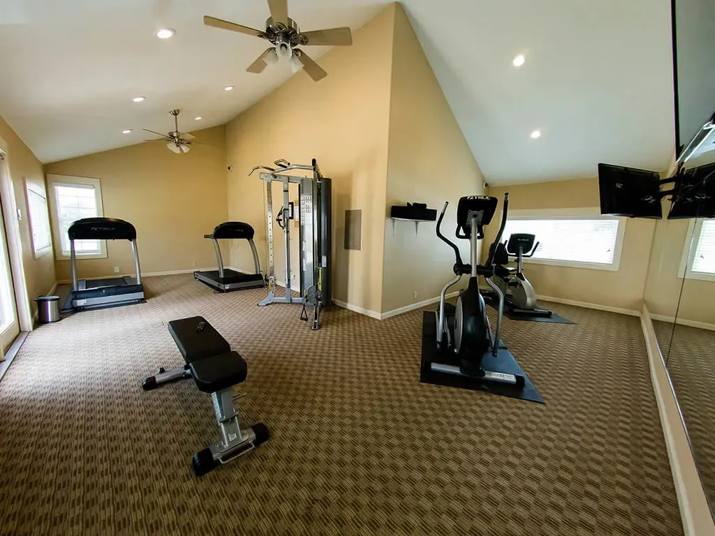 Treadmills, ellipticals, and weight machine in a spacious fitness center with ceiling fans.