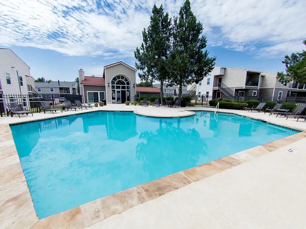 Resort-style swimming pool with lounge chairs and buildings in the background.