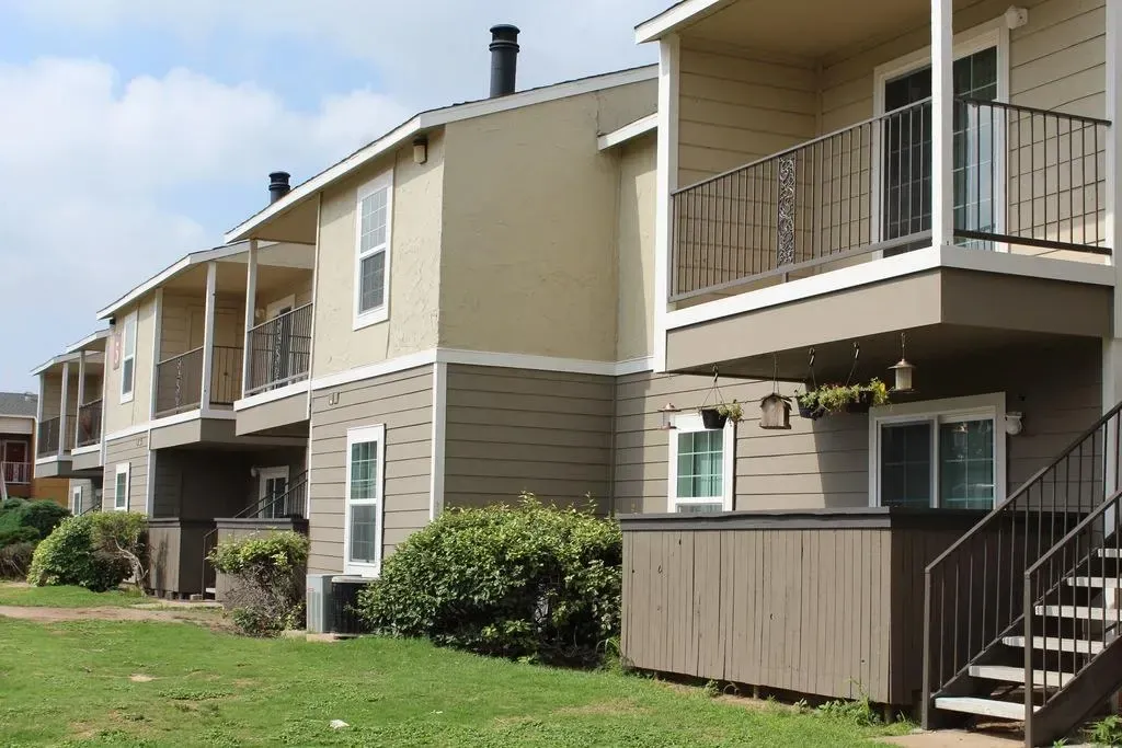 Exterior view of apartment buildings with balconies and grass.
