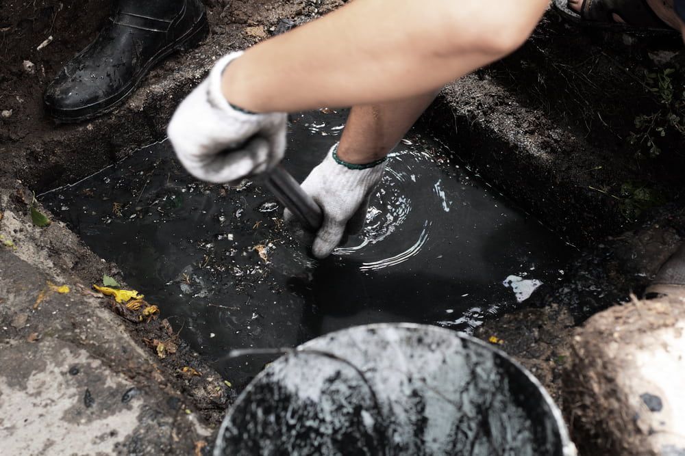 A Person Is Cleaning A Hole In The Ground With A Bucket Of Water — Nudges Plumbing In Dubbo, NSW