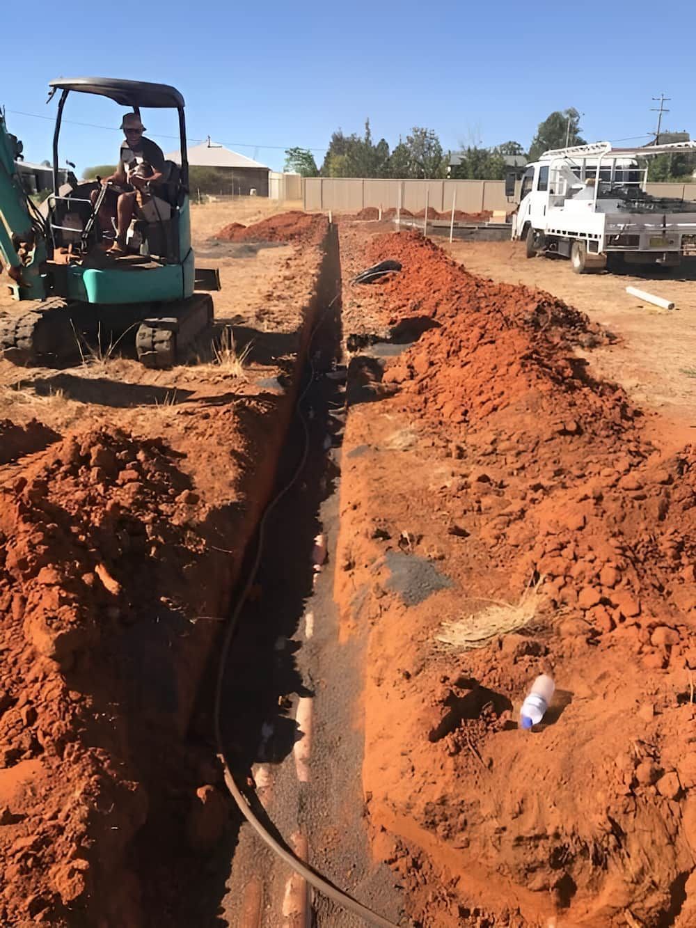 A Man Is Driving A Green Excavator In A Dirt Field — Nudges Plumbing In Dubbo, NSW