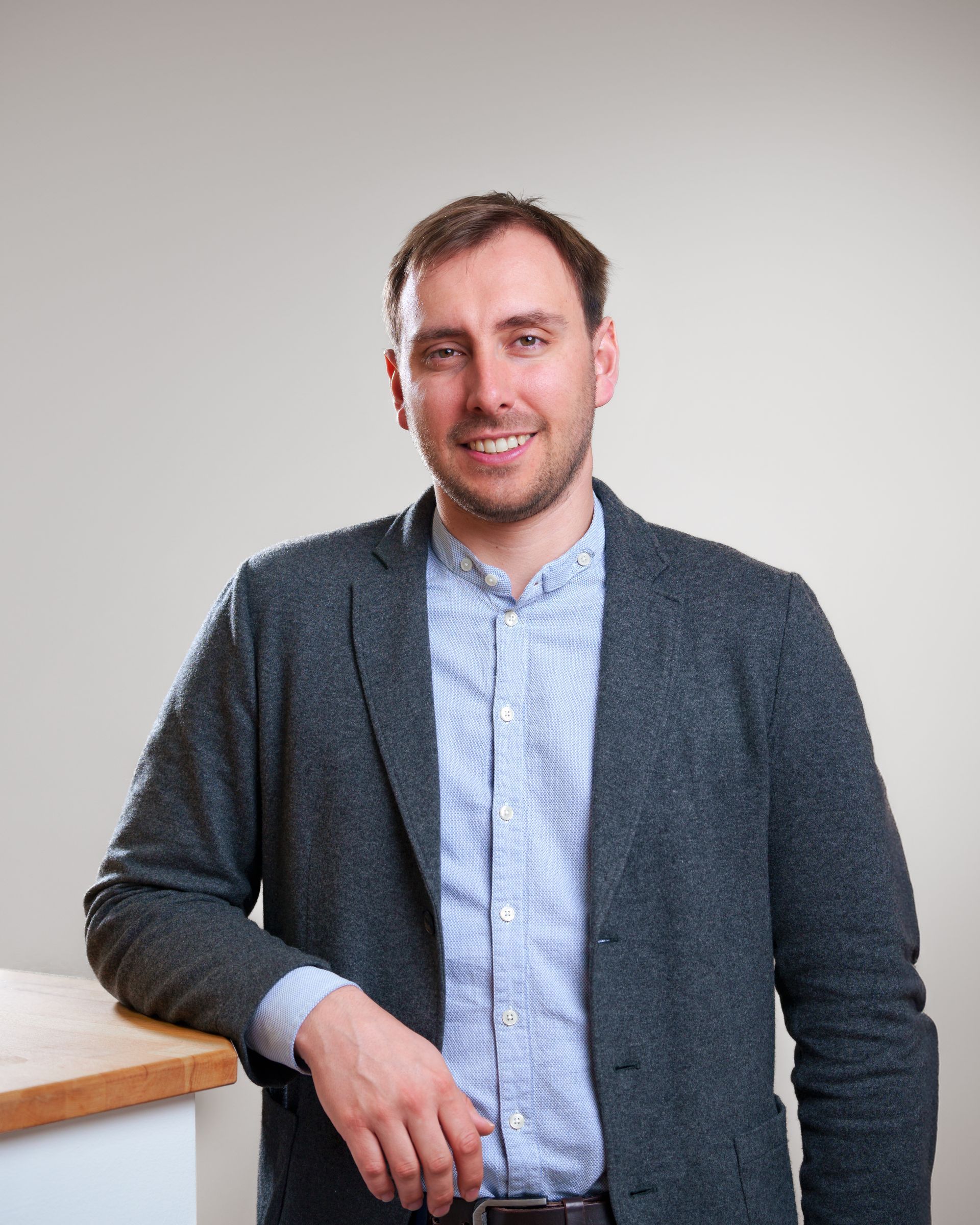 A man with a beard is standing next to a wooden table.