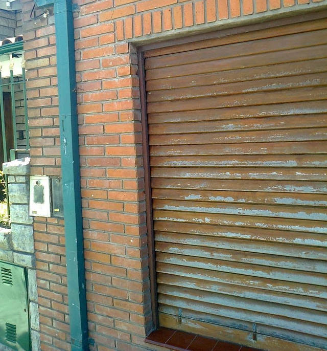 Fachada de un edificio de ladrillo con una persiana metálica marrón cerrada
