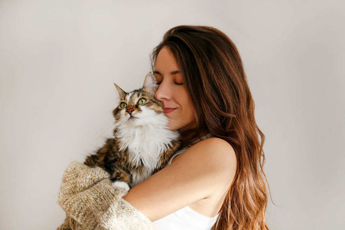 Woman holding a fluffy cat close, eyes closed, against a light background