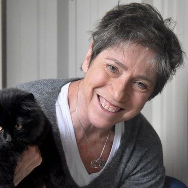 Smiling woman with short gray hair holding a black cat indoors