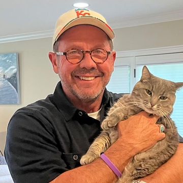 Smiling man in a cap holding a tabby cat indoors