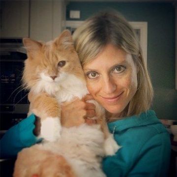Woman in teal holding a fluffy orange-and-white cat, both looking at the camera.