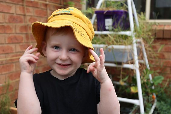 A young boy wearing a yellow hat is standing in front of a ladder.