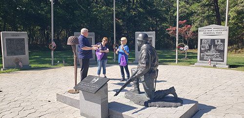 Group of people looking at a war memorial statue, trees in the background.