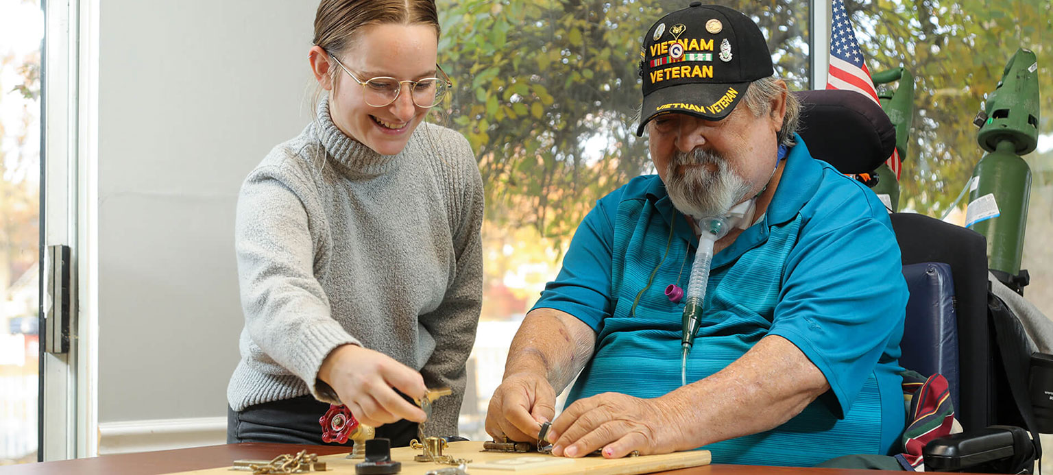 A woman is helping a man in a wheelchair with a project.