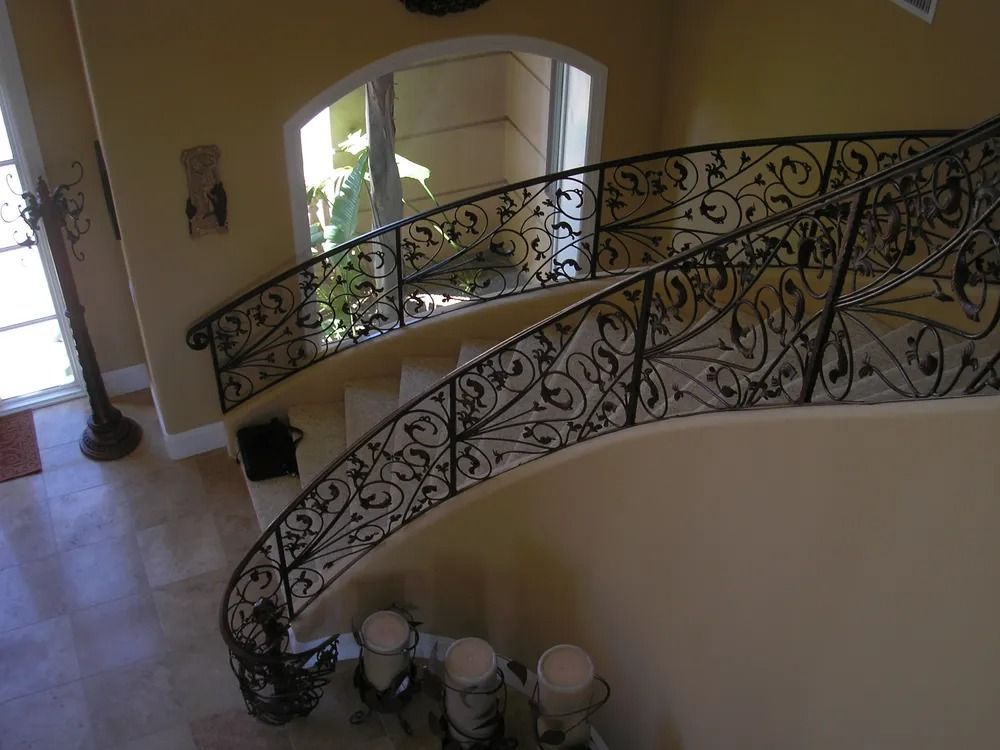 Ornate wrought iron railing on a curving staircase, cream walls, and tile flooring.