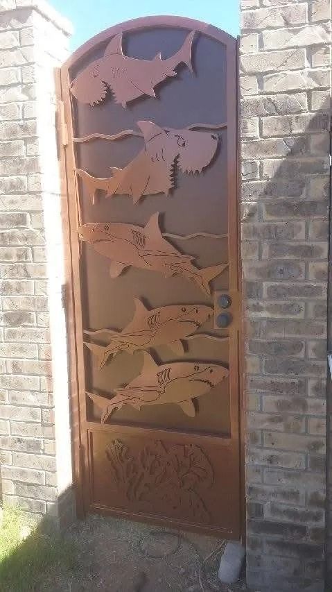 Metal gate with shark cutouts; brown finish, arched top, set in brick pillars.