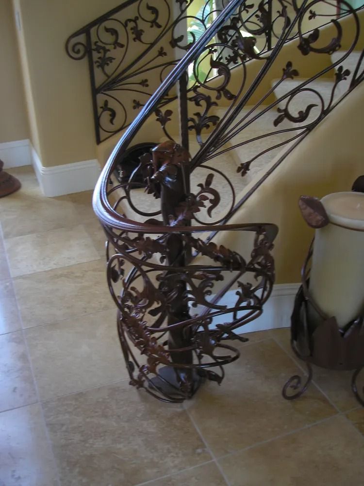 Ornate wrought iron spiral staircase in a home with beige walls and floor tiles.