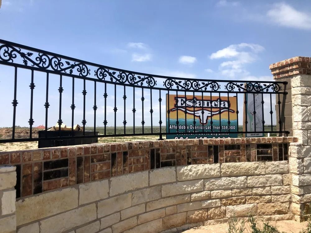 Black iron fence with decorative scrolls atop brick and stone entry to 