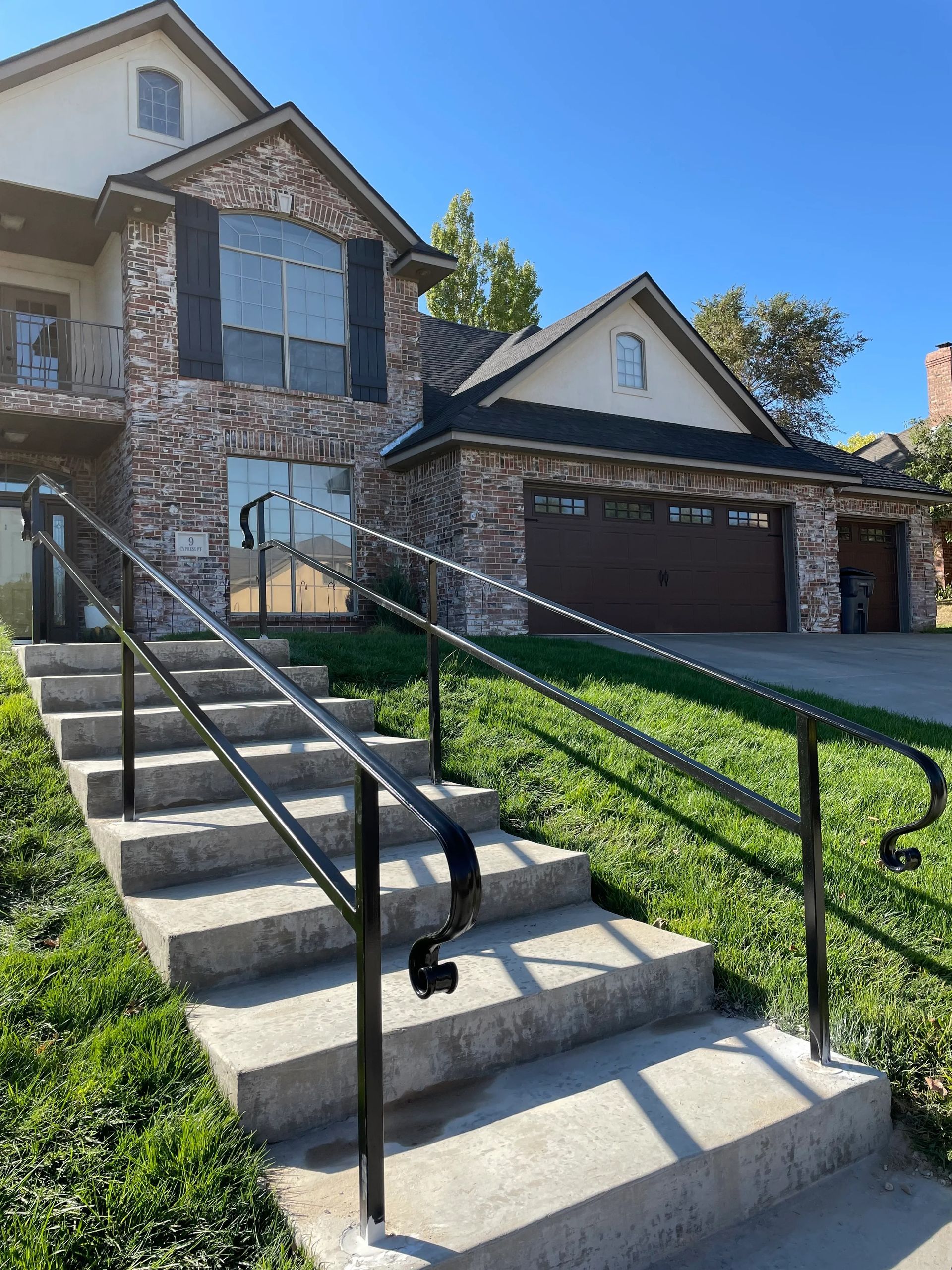 Exterior view of a two-story house with a stone facade, concrete steps, and black handrails. Green lawn.