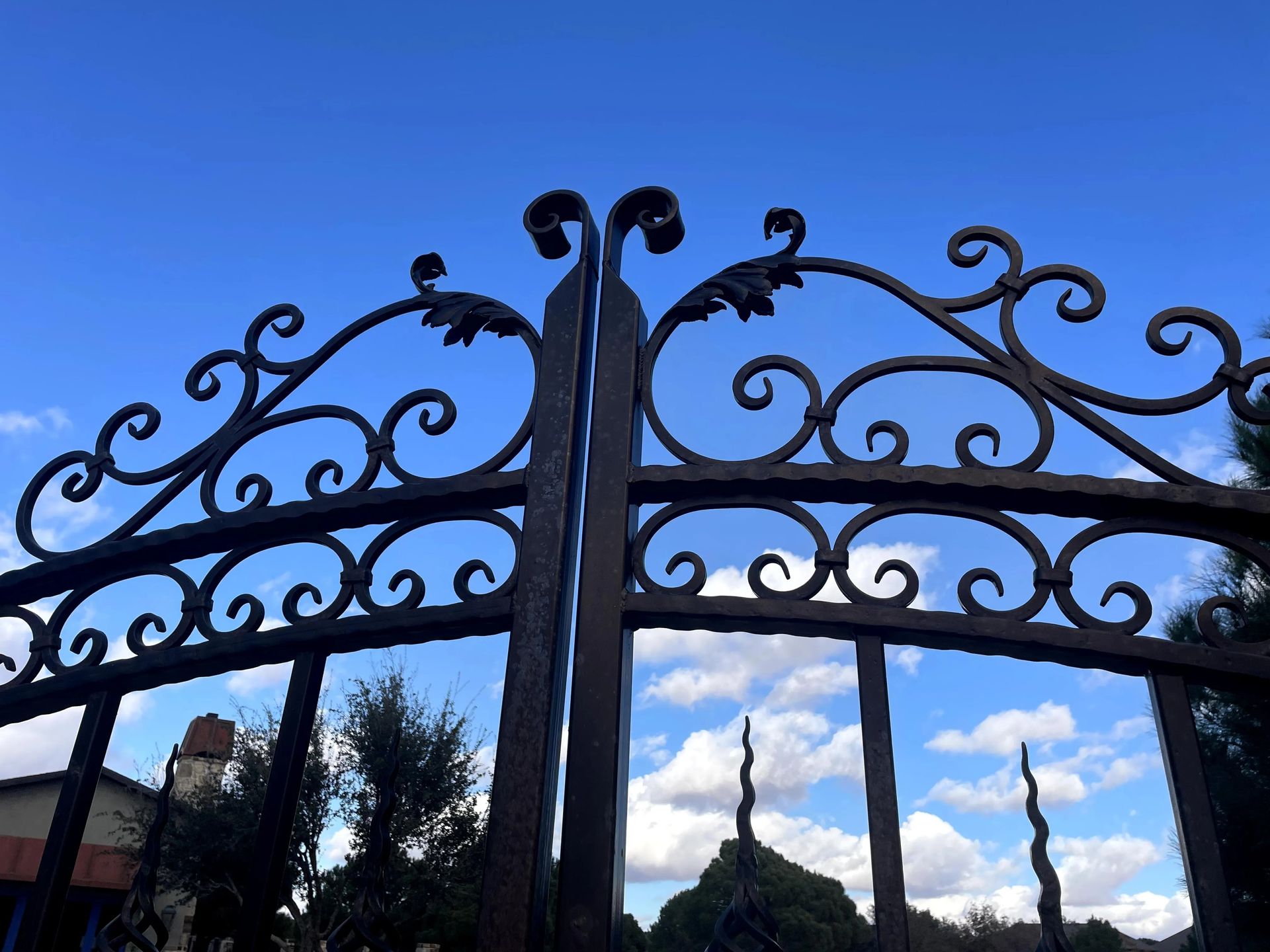 Ornate, dark metal gate against a partly cloudy, blue sky.