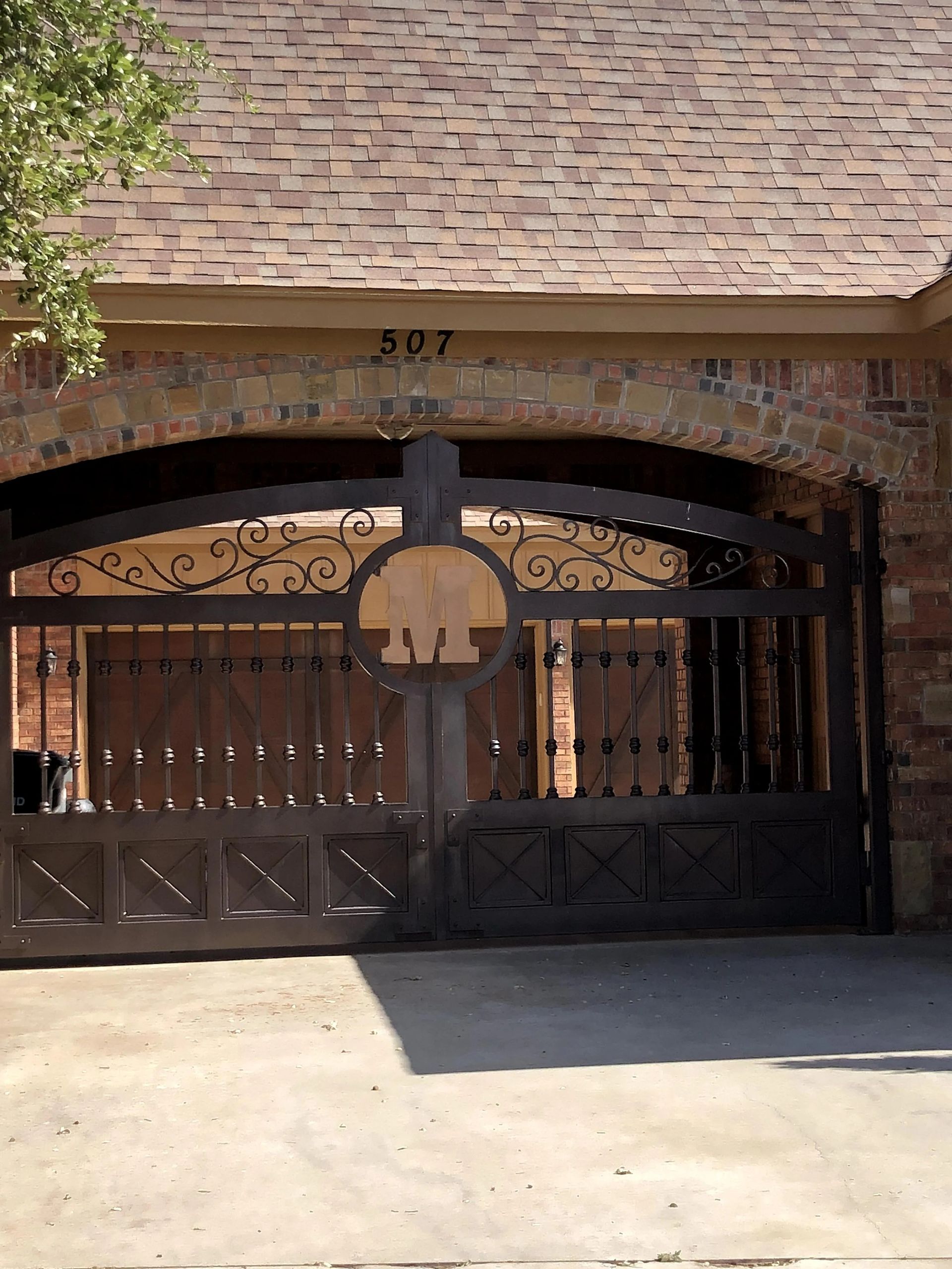 Brown brick arched driveway gate with ornate metalwork and address 