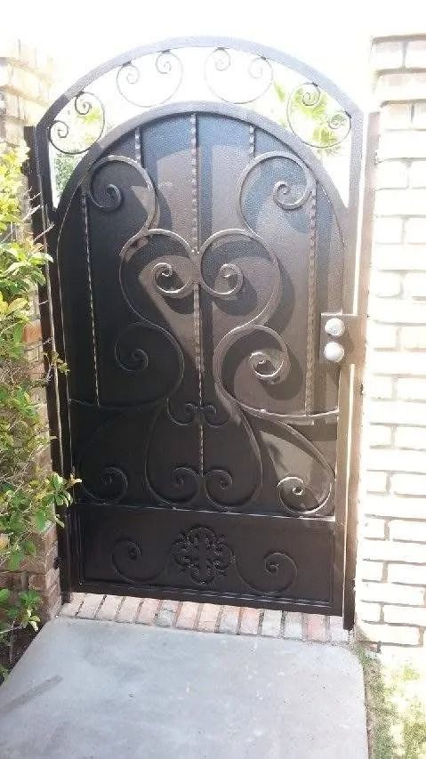Black wrought iron gate with decorative scrollwork, set into a brick wall.