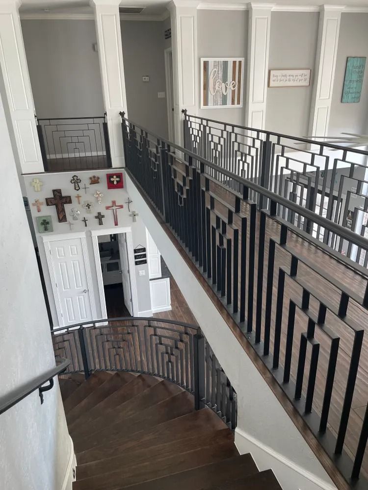Staircase with geometric black railing and dark wood steps, leading from a second-story hallway. White walls, artwork.