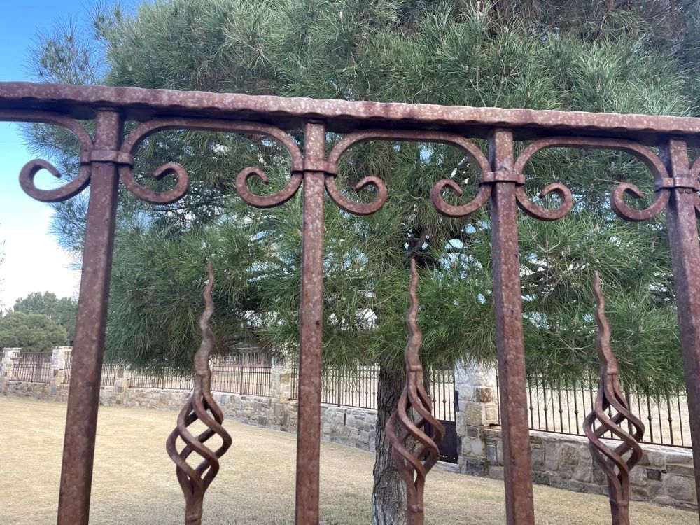 Rusty wrought iron fence with decorative swirls and a tree in the background.