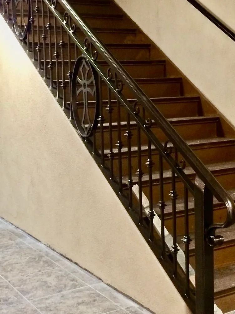 Staircase with wooden steps and ornate black metal railing, against a beige wall.