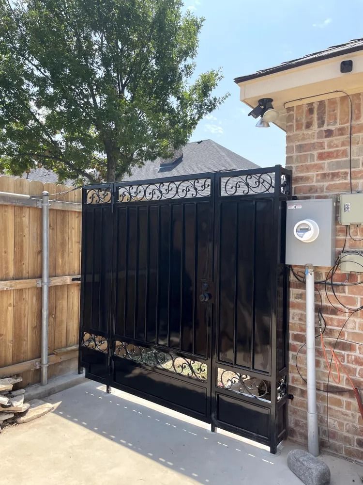 Black metal gate, bordering a brick wall and wooden fence, with an electrical box.