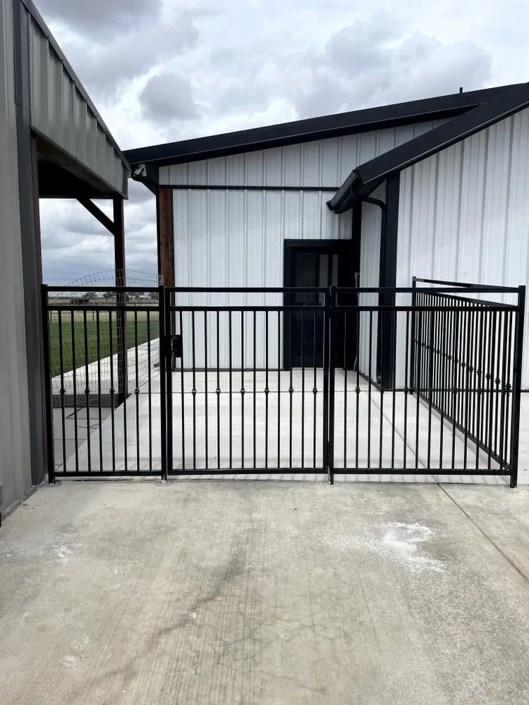 Black metal fence enclosing a concrete patio area, next to a white building.