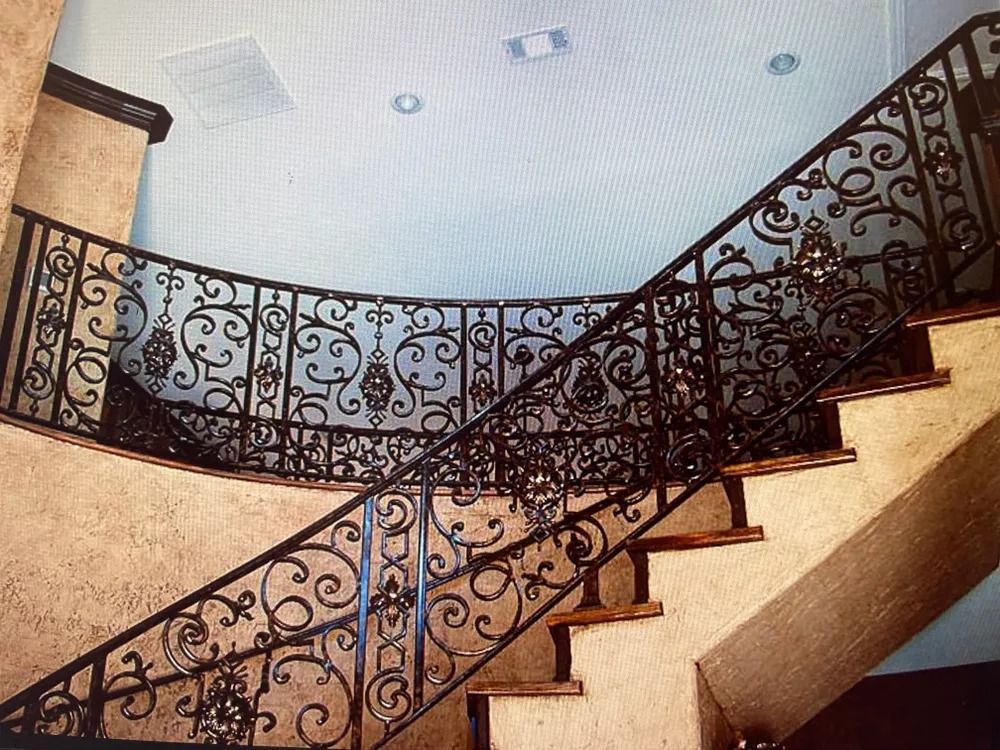 Ornate wrought iron railing on a curving staircase with wooden steps, against textured beige walls.