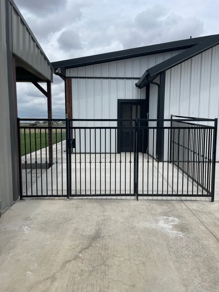 Black metal fence enclosing a concrete patio area, next to a white building.