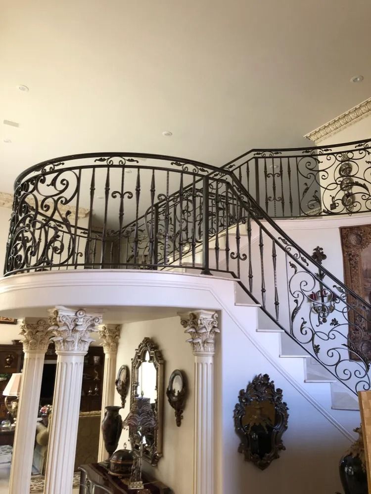 Elegant staircase with ornate wrought iron railings, white pillars, and decorative wall mirrors.