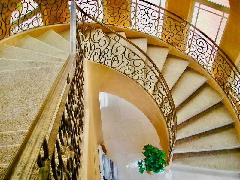 Spiral staircase with ornate wrought iron railing and beige carpet.