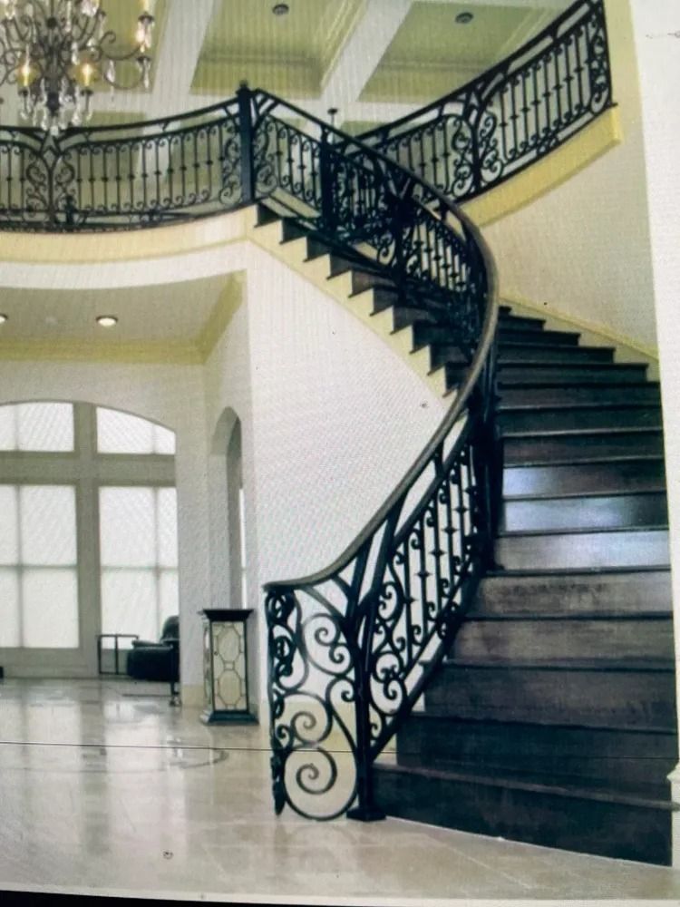 Elegant curved staircase with dark wood steps and ornate black wrought iron railing in a large, bright foyer.
