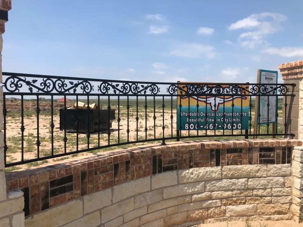 Black metal fence with decorative top, built on brick wall, with open land background.
