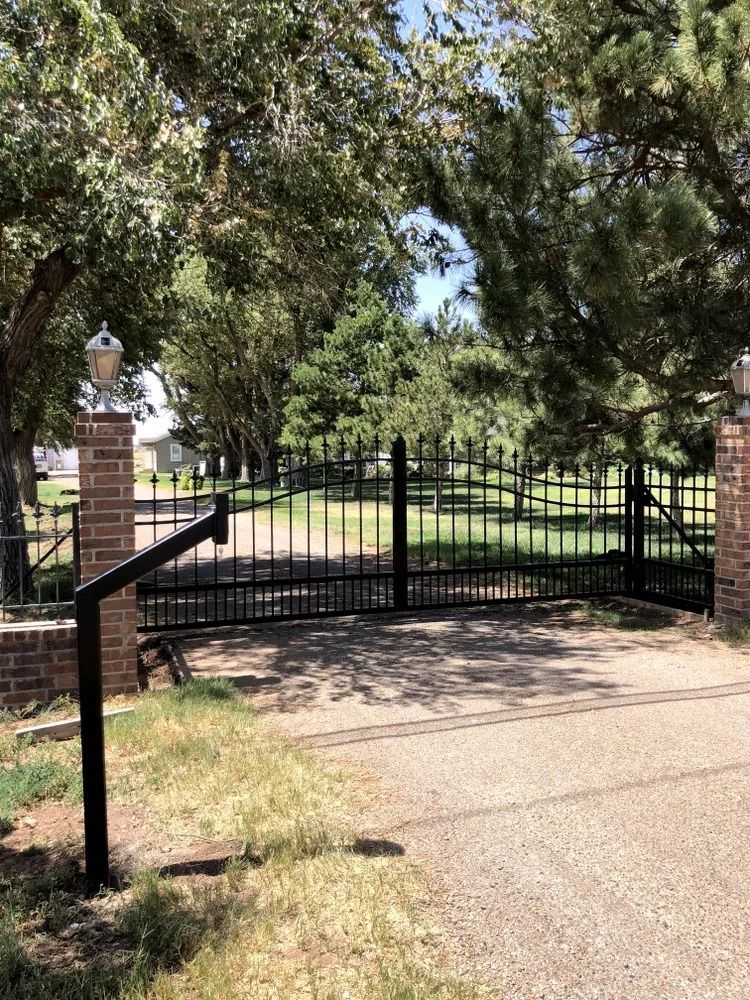 Black wrought iron gate with brick pillars and a lamp.